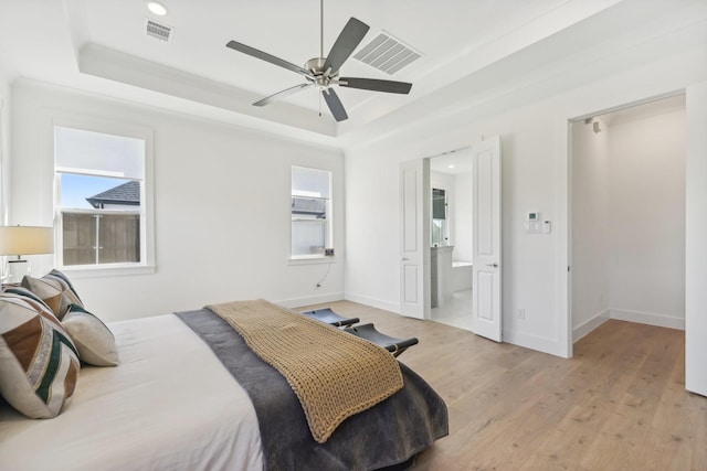 bedroom featuring light wood finished floors, a tray ceiling, multiple windows, and visible vents