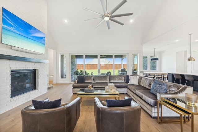 living room with ceiling fan, high vaulted ceiling, light hardwood / wood-style flooring, and a fireplace