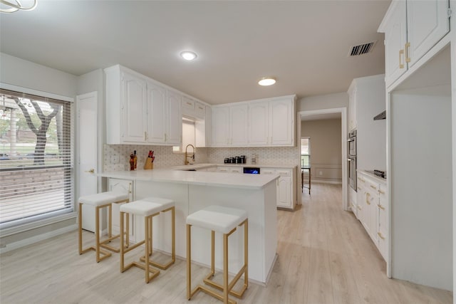 kitchen with a kitchen bar, light hardwood / wood-style floors, white cabinetry, and kitchen peninsula