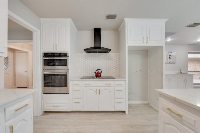 kitchen with white cabinets, light stone countertops, double oven, and wall chimney exhaust hood