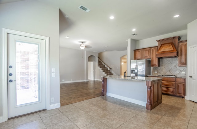 kitchen featuring appliances with stainless steel finishes, custom exhaust hood, a healthy amount of sunlight, and an island with sink