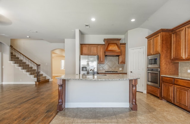 kitchen with light stone counters, a center island with sink, stainless steel appliances, and tasteful backsplash