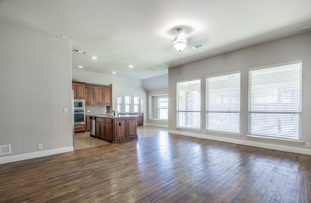 kitchen with appliances with stainless steel finishes, hardwood / wood-style flooring, decorative backsplash, sink, and a center island with sink