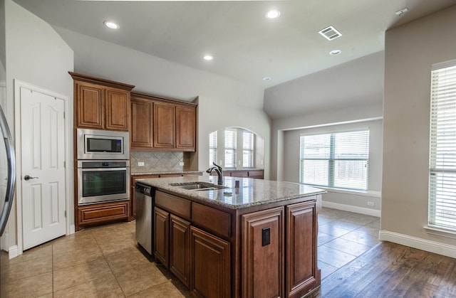 kitchen with sink, light stone counters, a center island with sink, decorative backsplash, and stainless steel appliances