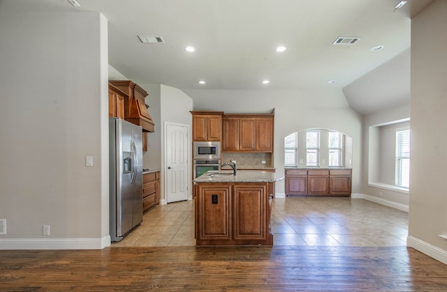 kitchen featuring light wood-type flooring, stainless steel appliances, a kitchen island with sink, and light stone countertops