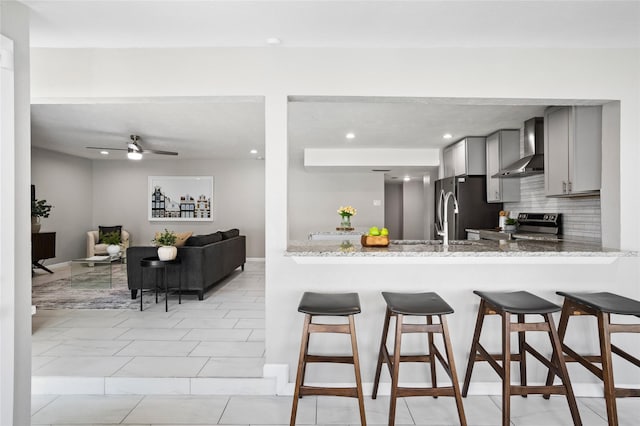 kitchen with appliances with stainless steel finishes, wall chimney exhaust hood, decorative backsplash, gray cabinets, and kitchen peninsula