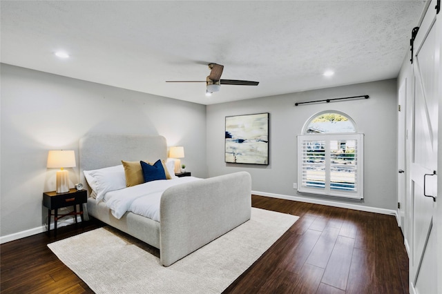 bedroom with dark hardwood / wood-style floors, ceiling fan, and a barn door