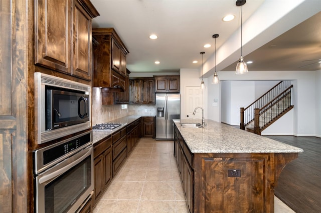 kitchen featuring appliances with stainless steel finishes, sink, backsplash, hanging light fixtures, and a kitchen island with sink