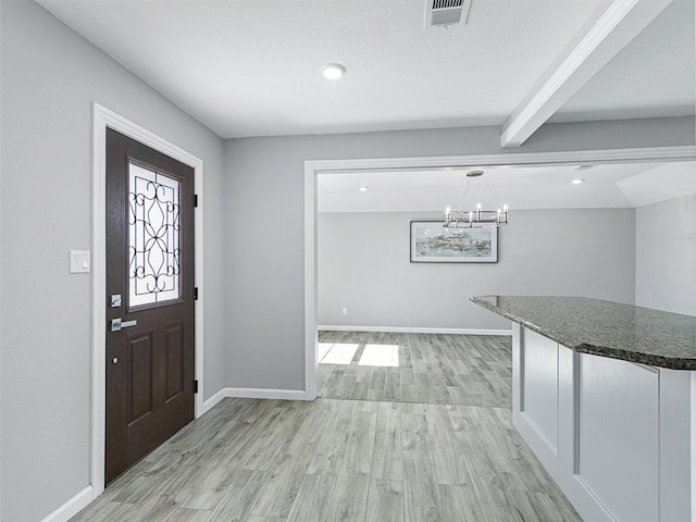 entryway with light wood-type flooring, a chandelier, and beam ceiling