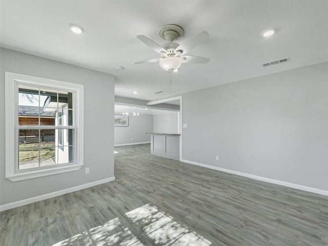 empty room with ceiling fan with notable chandelier and wood-type flooring