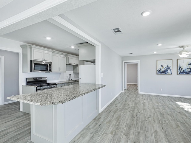 kitchen with appliances with stainless steel finishes, a kitchen bar, light hardwood / wood-style floors, ceiling fan, and light stone counters