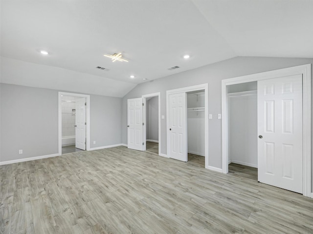 unfurnished bedroom featuring lofted ceiling, multiple closets, ensuite bath, and light wood-type flooring