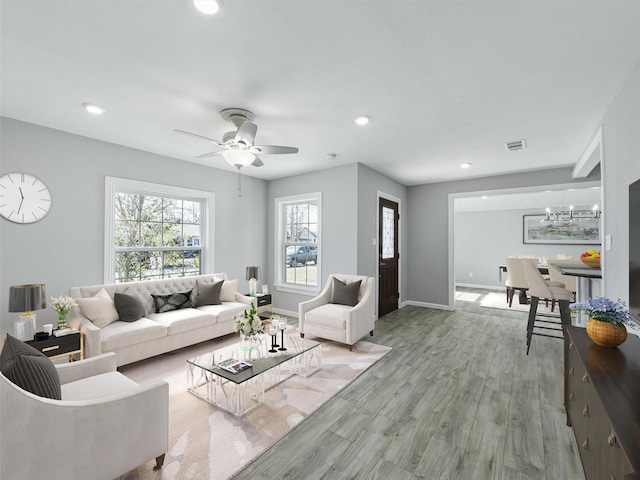 living room with light wood-type flooring and ceiling fan with notable chandelier