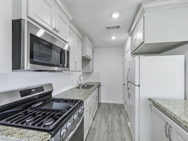 kitchen featuring sink, light stone counters, white cabinets, and stainless steel appliances