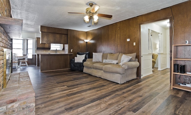 living room featuring dark hardwood / wood-style floors, wood walls, sink, ceiling fan, and a textured ceiling