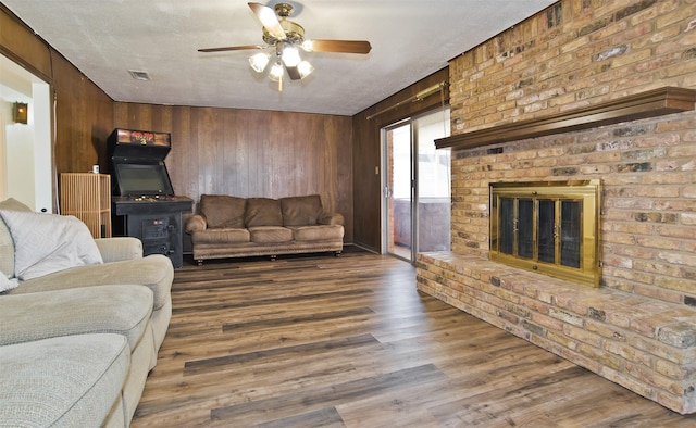 living room with wooden walls, a fireplace, wood-type flooring, ceiling fan, and a textured ceiling