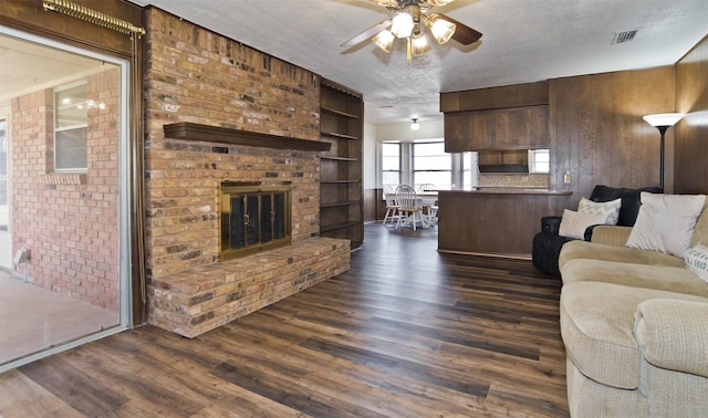 living room featuring ceiling fan, dark hardwood / wood-style floors, a brick fireplace, and a textured ceiling