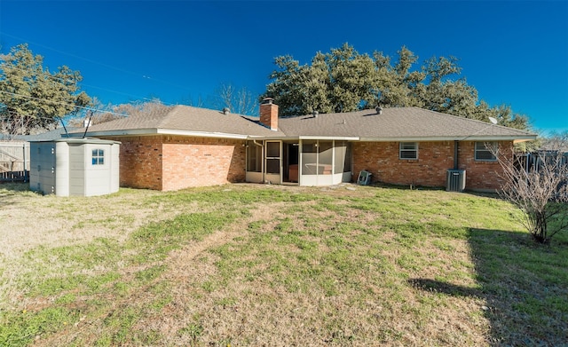 rear view of property featuring a storage shed, central AC unit, a lawn, and a sunroom