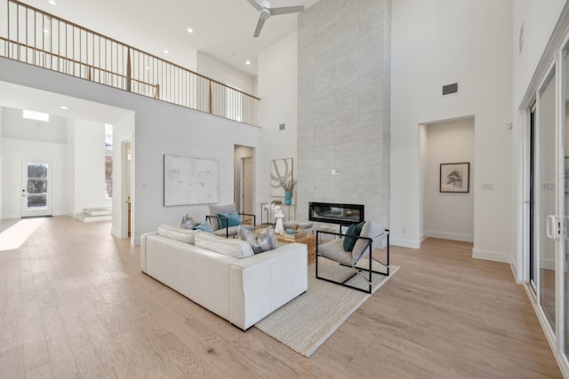 living area with light wood-style flooring, a high ceiling, a fireplace, visible vents, and baseboards