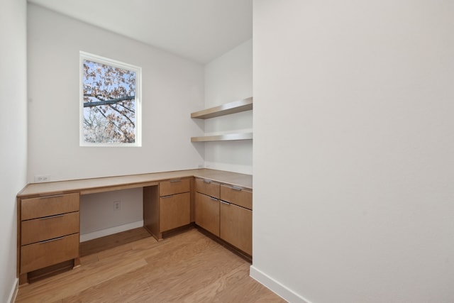 unfurnished office featuring light wood-type flooring, built in desk, and baseboards