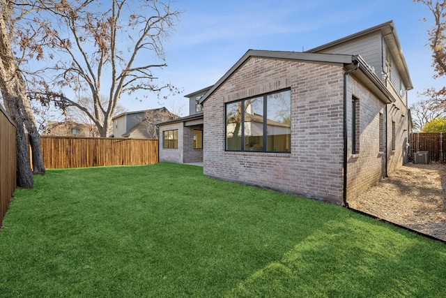 rear view of house featuring brick siding, a yard, a fenced backyard, and central air condition unit