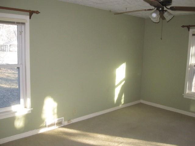 carpeted spare room featuring ceiling fan and a wealth of natural light