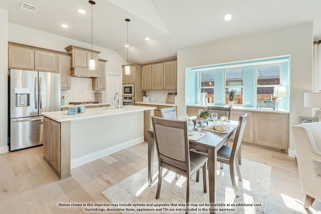 kitchen featuring pendant lighting, vaulted ceiling, an island with sink, decorative backsplash, and stainless steel appliances