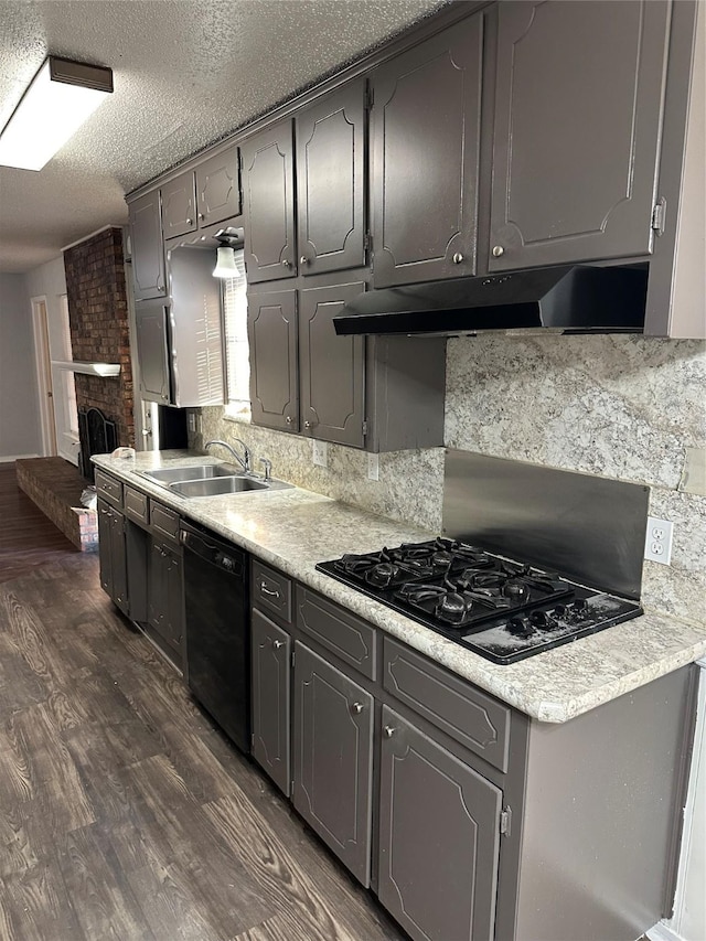 kitchen featuring sink, backsplash, dark hardwood / wood-style floors, black appliances, and a brick fireplace