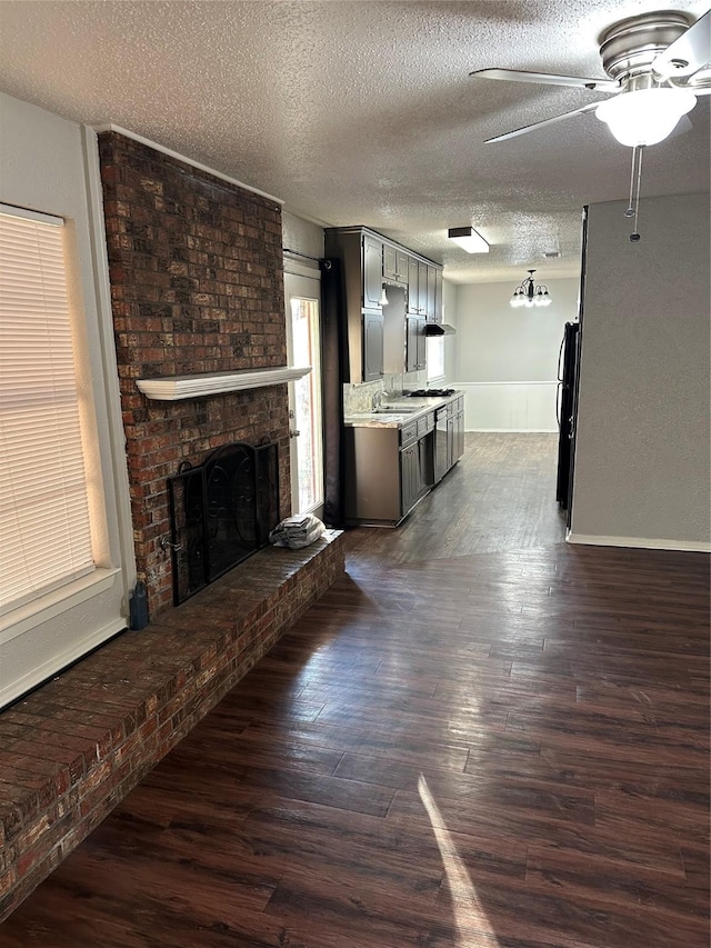 unfurnished living room featuring dark wood-type flooring, ceiling fan, a brick fireplace, and a textured ceiling