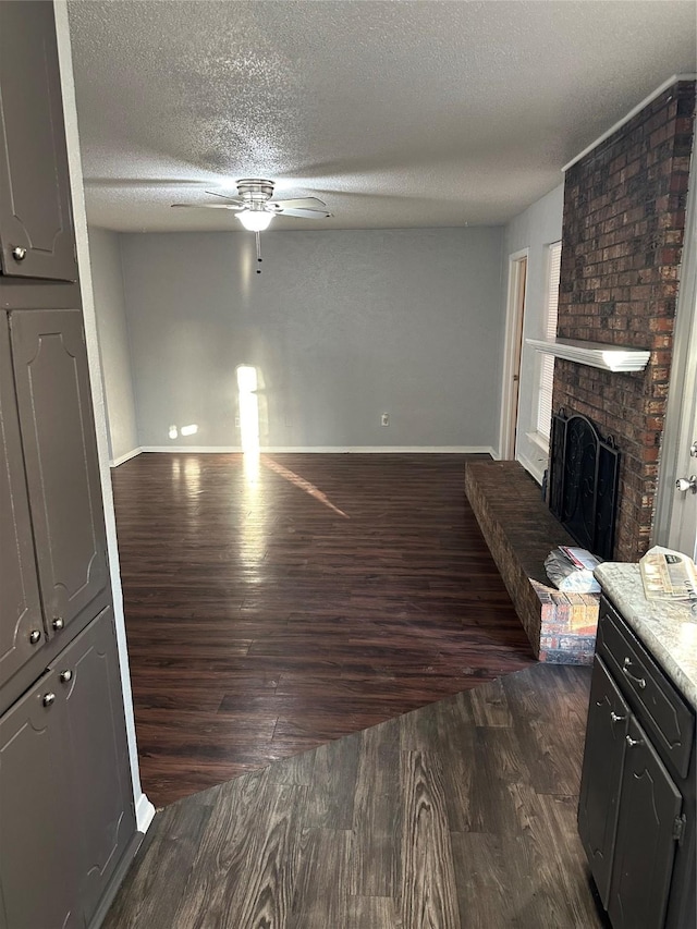 living room with ceiling fan, a fireplace, dark hardwood / wood-style floors, and a textured ceiling