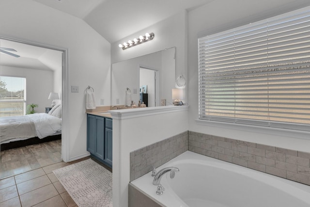 bathroom with tile patterned floors, vanity, tiled bath, vaulted ceiling, and ceiling fan