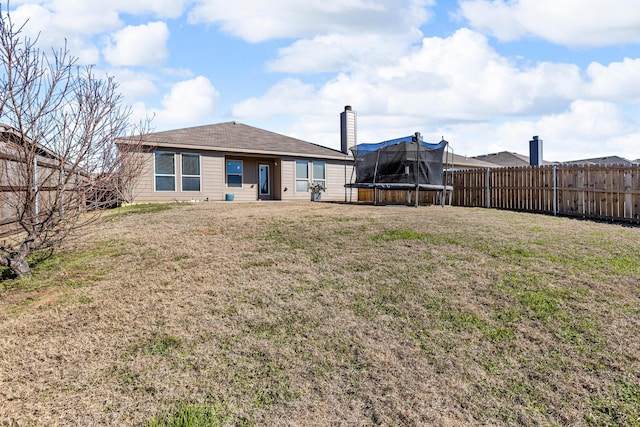 rear view of house featuring a trampoline and a lawn