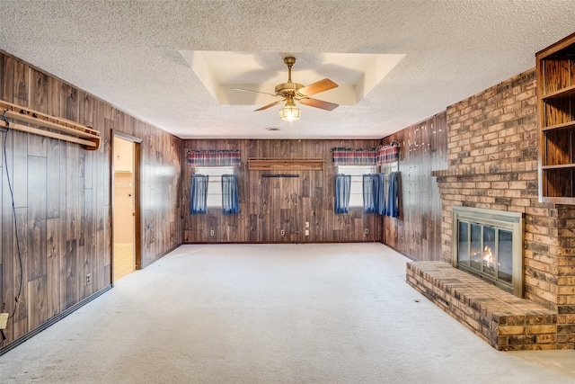 unfurnished living room with ceiling fan, light colored carpet, a brick fireplace, a textured ceiling, and wooden walls