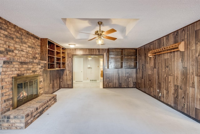 unfurnished living room featuring a brick fireplace, a textured ceiling, light carpet, and wooden walls