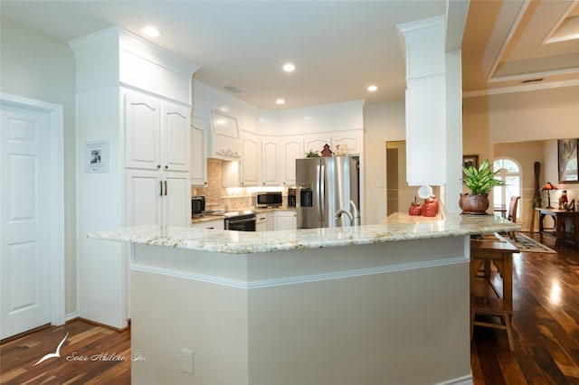 kitchen with light stone countertops, white cabinets, appliances with stainless steel finishes, a kitchen bar, and kitchen peninsula