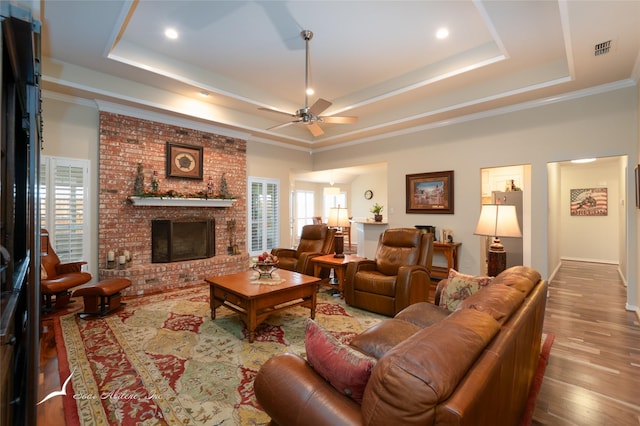 living room featuring a fireplace, hardwood / wood-style flooring, a raised ceiling, and ornamental molding