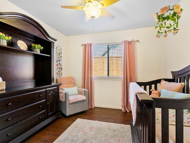 bedroom featuring ceiling fan, dark hardwood / wood-style flooring, and a crib