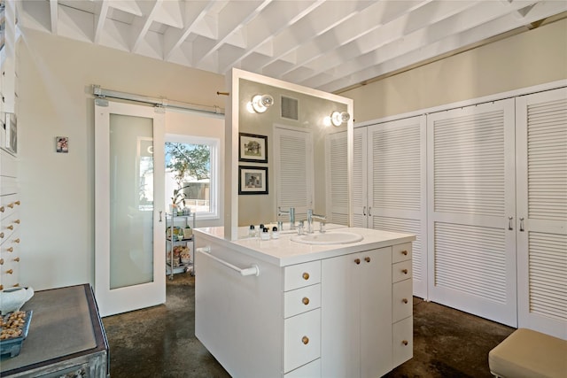 interior space with white cabinetry, a barn door, sink, and a center island with sink