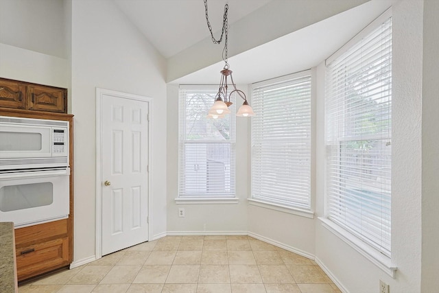 kitchen with a notable chandelier, white appliances, hanging light fixtures, light tile patterned floors, and lofted ceiling