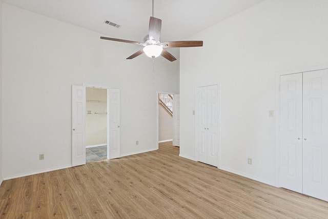 unfurnished bedroom featuring multiple closets, light wood-type flooring, high vaulted ceiling, and ceiling fan