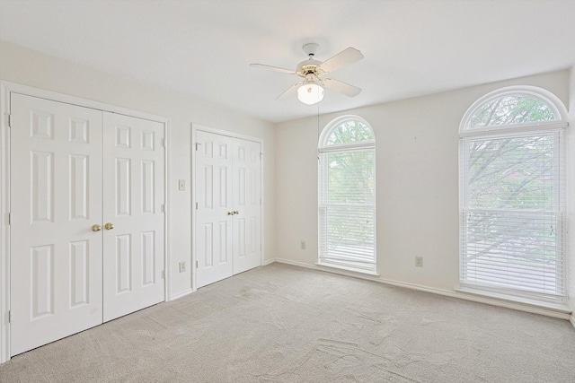 unfurnished bedroom with multiple closets, ceiling fan, light carpet, and multiple windows