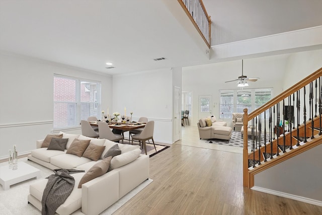 living room with crown molding, light wood-type flooring, a high ceiling, and plenty of natural light