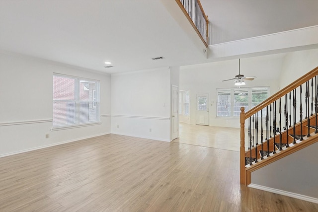 living room with a high ceiling, ceiling fan, a healthy amount of sunlight, and light hardwood / wood-style flooring