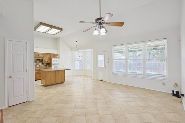 kitchen featuring hanging light fixtures, backsplash, ceiling fan with notable chandelier, a center island, and lofted ceiling