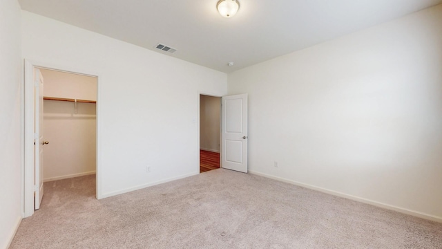 unfurnished bedroom featuring a walk in closet, light carpet, and a closet