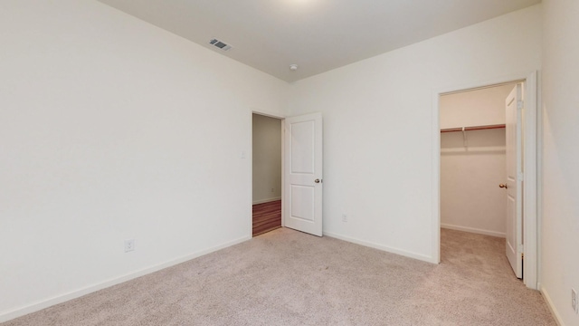 unfurnished bedroom with a walk in closet, light colored carpet, and a closet