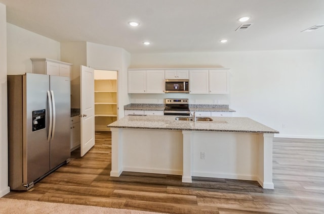 kitchen featuring appliances with stainless steel finishes, white cabinetry, sink, light stone counters, and a center island with sink