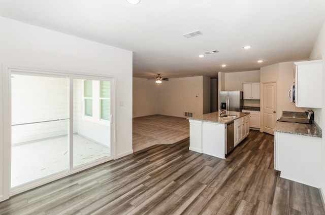 kitchen featuring appliances with stainless steel finishes, white cabinets, an island with sink, light stone counters, and dark hardwood / wood-style floors