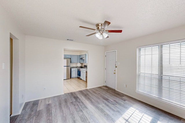 unfurnished living room with ceiling fan, light hardwood / wood-style flooring, and a textured ceiling