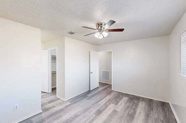 unfurnished bedroom featuring light hardwood / wood-style flooring, ceiling fan, a textured ceiling, a walk in closet, and a closet